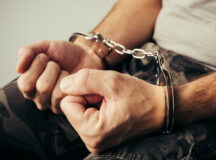 Handcuffed soldier in military army clothes. Prisoner of war or arrested terrorist, close up of hands in handcuffs, selective focus.